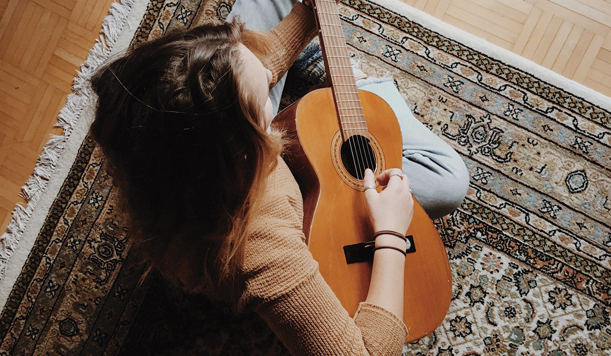 woman sitting on a rug playing guitar strings