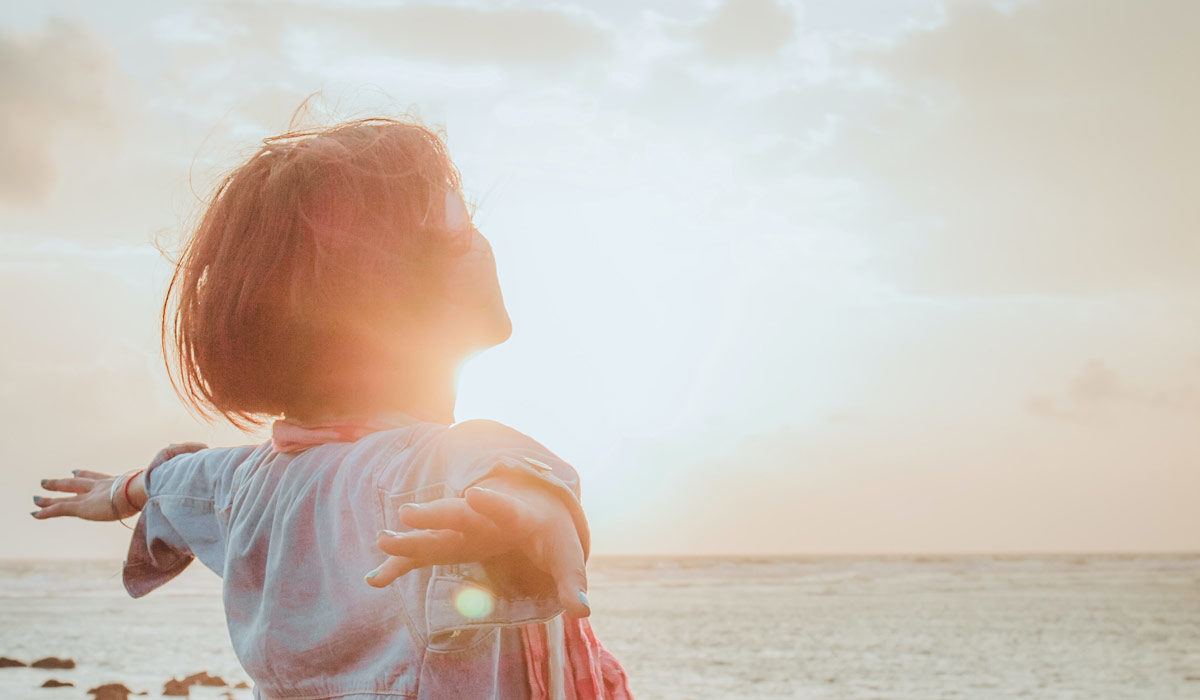 a girl facing the ocean with her arms spread out