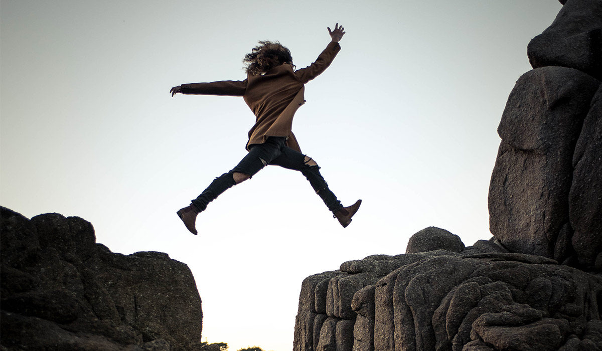 a silhouette of a person jumping between rocks