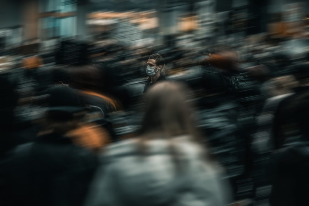 a person with a mask on walking in a sea of blurred people