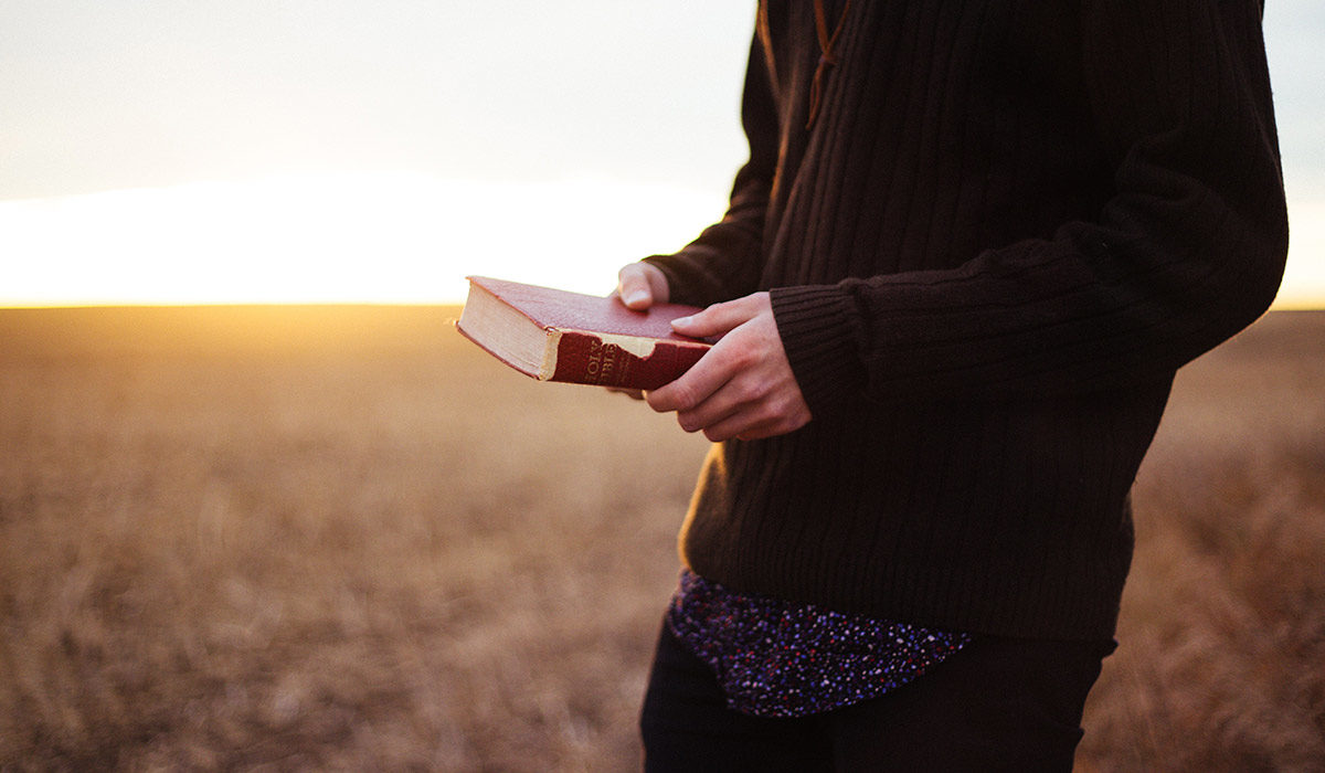 a man holding a bible and standing in a field