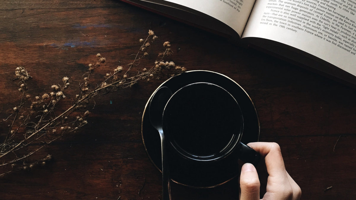 a hand holding a black ceramic mug of coffee on a saucer