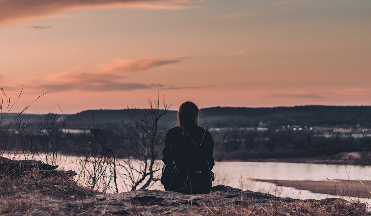 a person sitting on a ledge and looking at the sunset