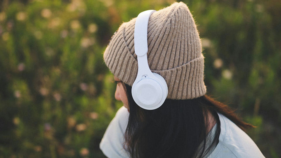 Healing from Sexual Abuse Audio Series, Person wearing a beige knit hat and white headphones, sitting outdoors and listening quietly in a peaceful natural setting.